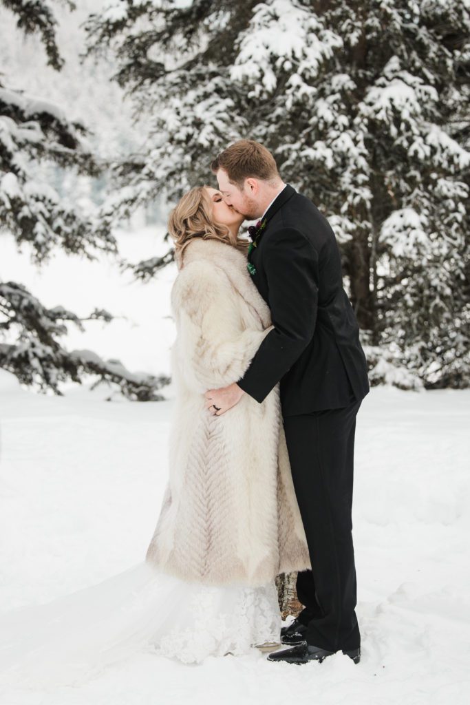 Bride and groom's first kiss during the outdoor magical winter wedding in Banff, with deep snow and stunning mountains