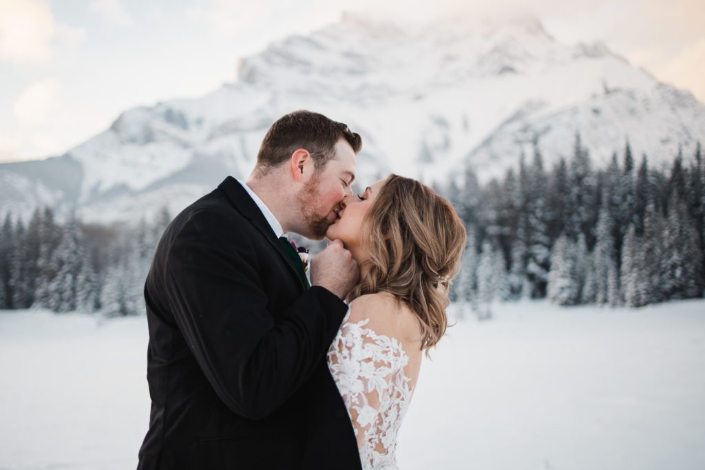 magical winter wedding in banff with mountain backdrop, lace sleeve dress, and rosy red cheeks from the cold air!